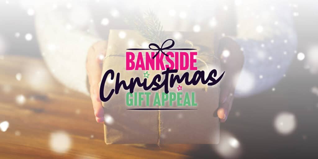 A person holding a wrapped Christmas gift with twine and a small pine sprig. Overlaid festive text reads “Bankside Christmas Gift Appeal” in bold pink, black, and green lettering, with a softly blurred snowy background.