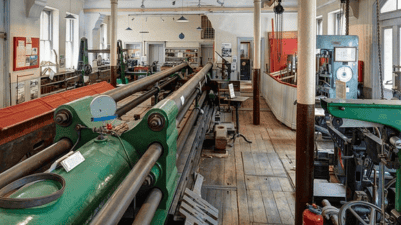 Interior of the Kirkaldy Testing Works showing large Victorian-era testing machines, metal equipment, and wooden floors in a historic workshop setting.